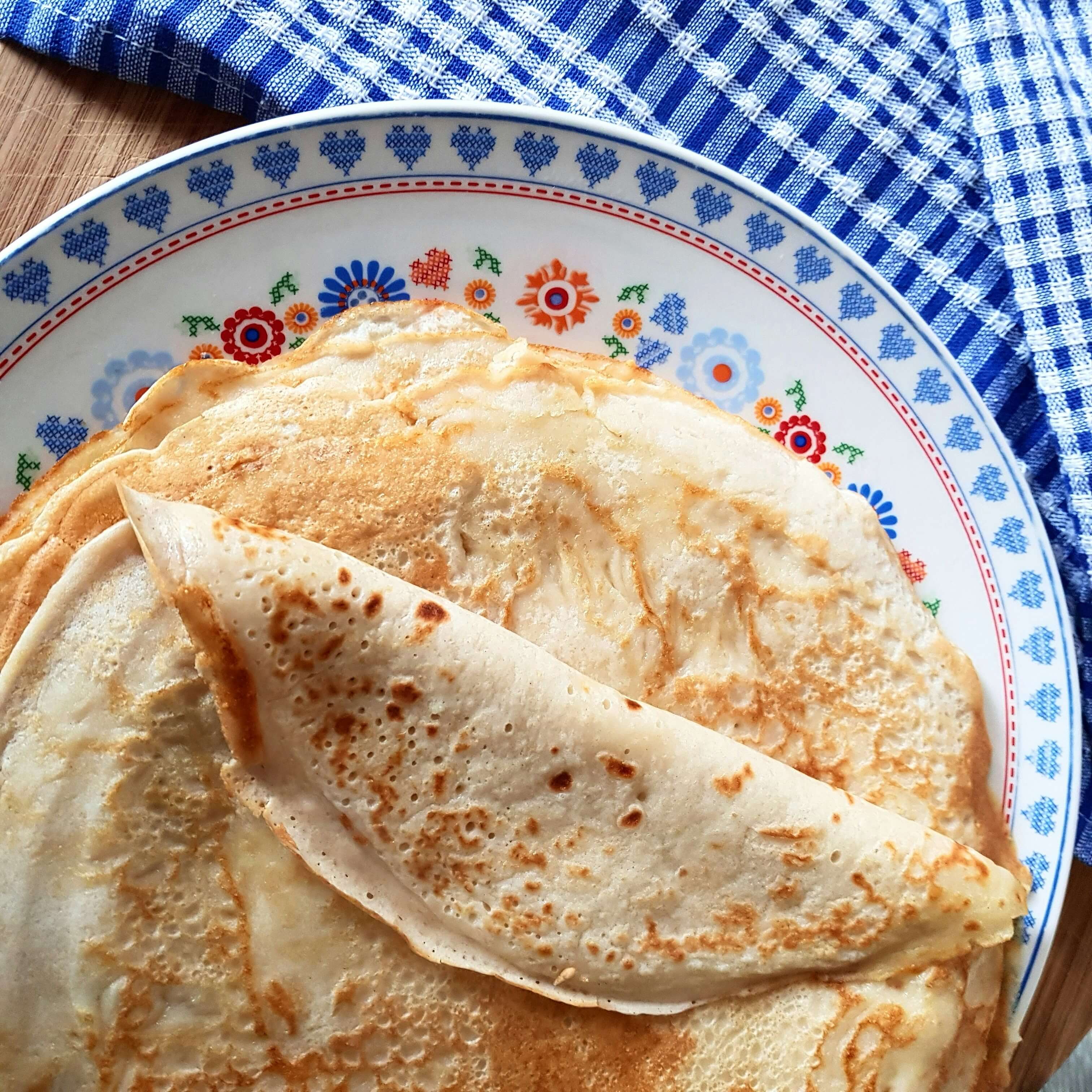 Crêpes maison empilées sur une assiette décorée, servies pour la Chandeleur sur une table avec un torchon bleu.